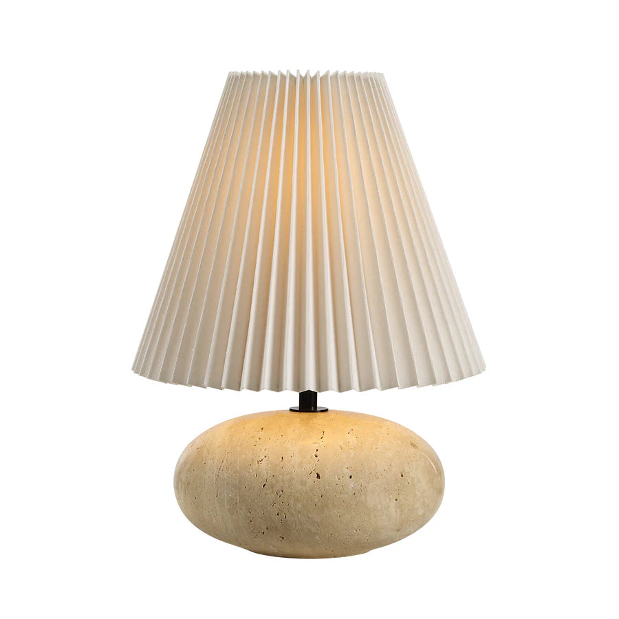 Table lamp with pleated beige shade and textured travertine base on a white background