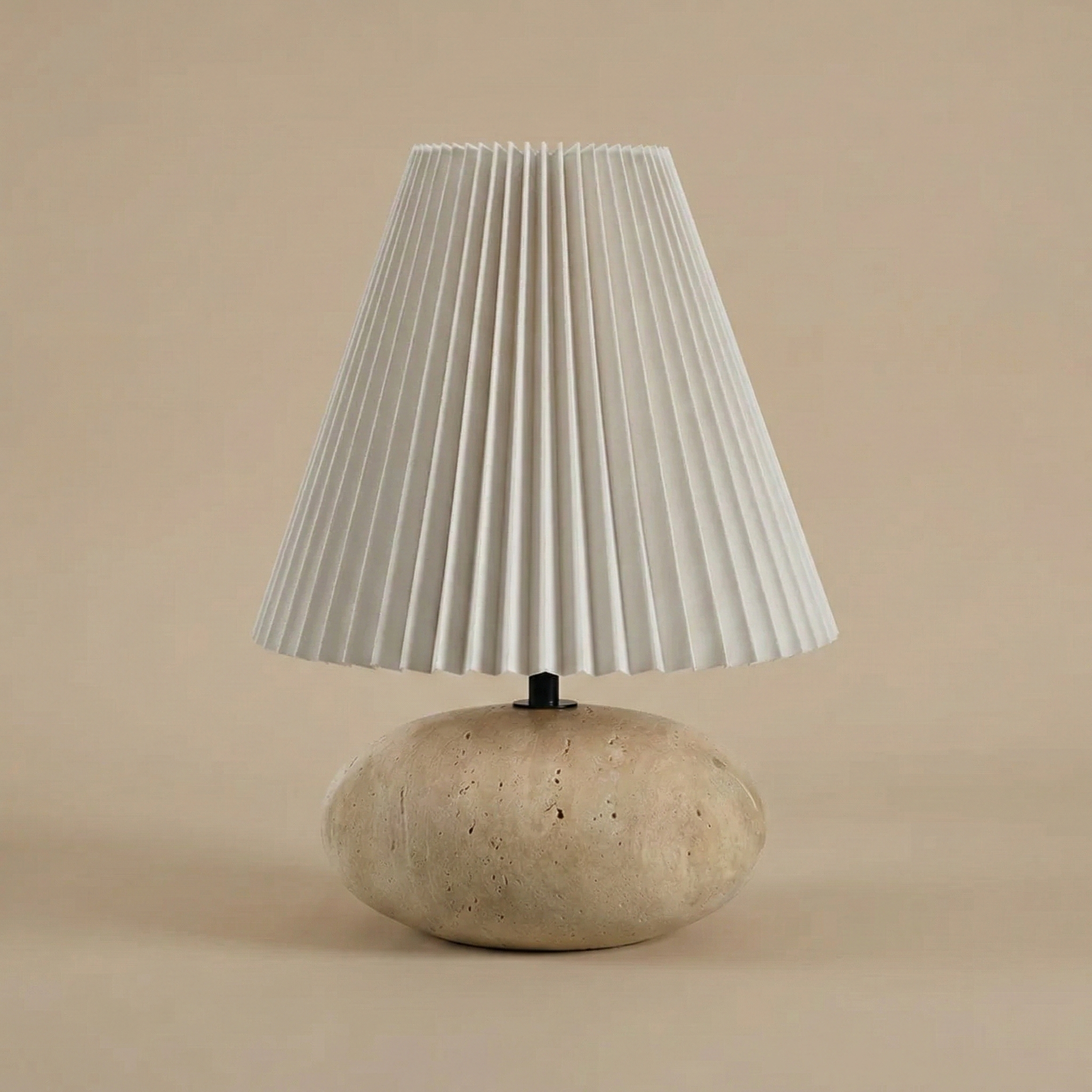 Table lamp with pleated white shade and travertine base on beige background