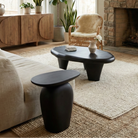 Organic black pebble tables styled in a bright rustic living room with a stone fireplace, jute rug, and rattan chairs.