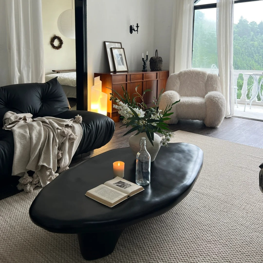 Pebble Coffee Table in matte black finish styled with black leather sofa, boucle chair, and soft neutral decor in cozy living room