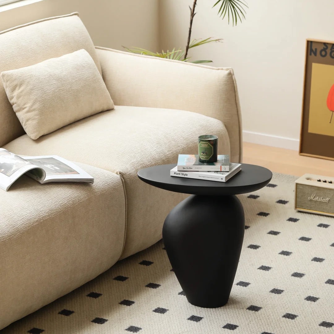 Pebble Side Table in matte black finish beside beige sofa, styled with books and candle in a bright minimal living room