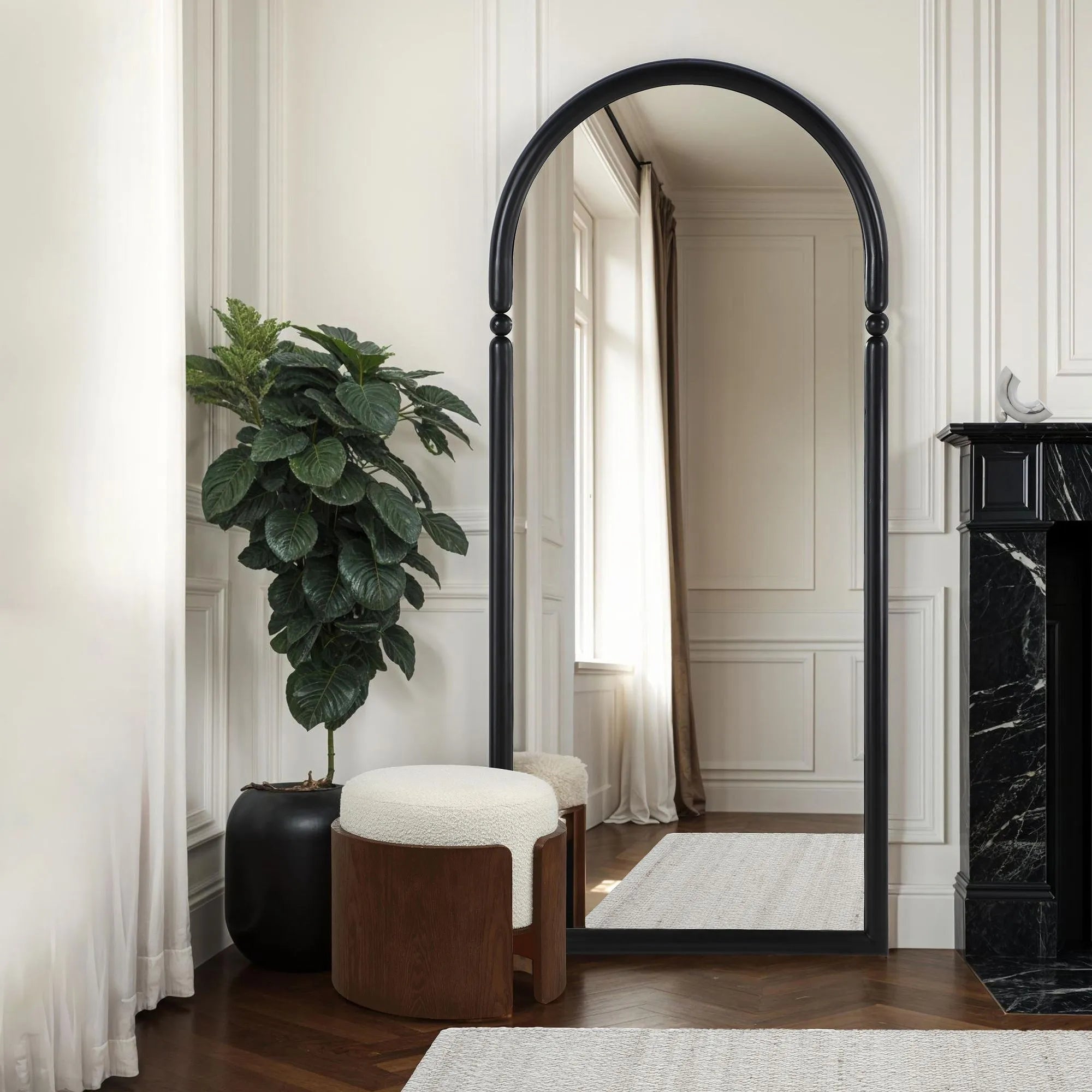 The Rondo white bouclé and dark wood vanity stool styled next to a tall black arched floor mirror and a large potted plant.