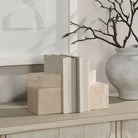 Sculptural geometric travertine bookends styled on a wooden sideboard holding white books, highlighting their functional weight and modern aesthetic.