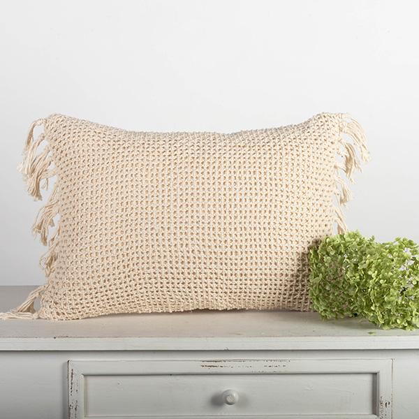 Woven pillow with tassels on a gray surface with a light background