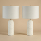 Two table lamps with white textured bases and white lampshades on a beige background