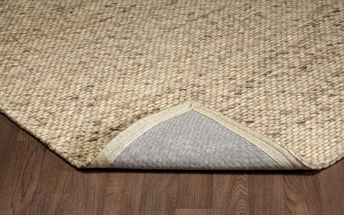 Folded corner of the beige Silas wool rug, revealing its chunky looped surface and sturdy backing.