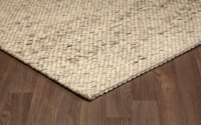 Corner view of the beige and cream Silas hand-woven wool rug laying flat on a hardwood floor.