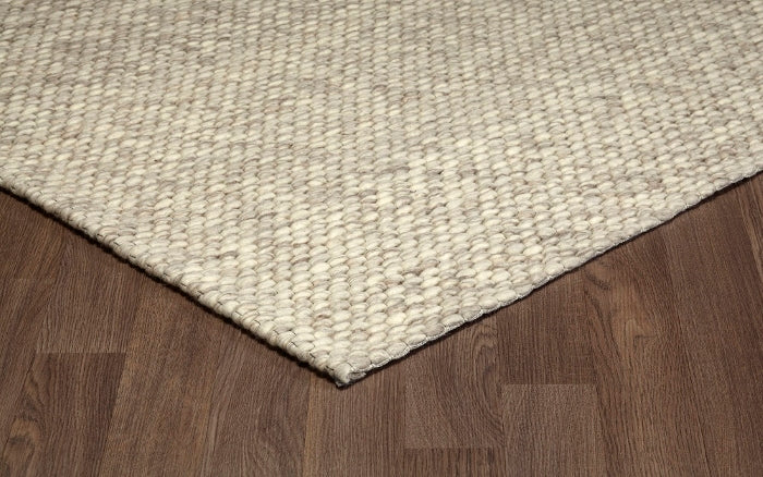 Corner view of the cream Silas hand-woven wool rug resting on a wooden floor, showcasing its textured edge.