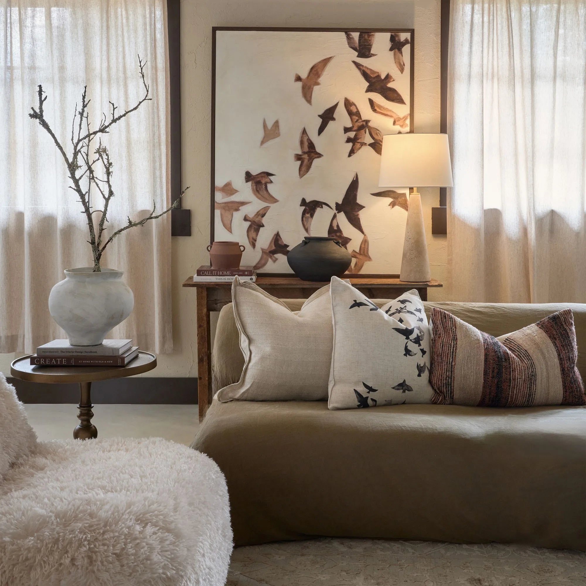 Large bird wall art styled in a neutral living room above a brown sofa with linen pillows.