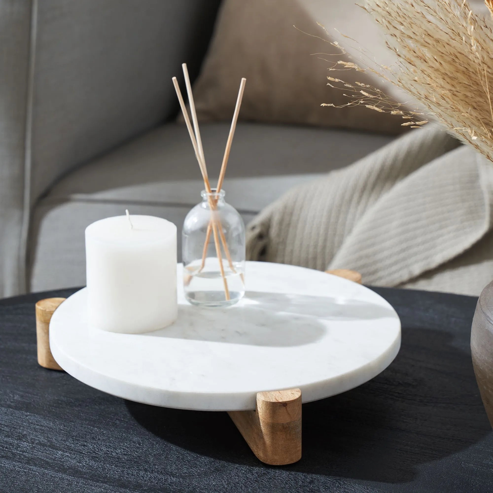 Siona Marble Tray styled with a white candle and glass diffuser on a dark coffee table beside a cozy sofa