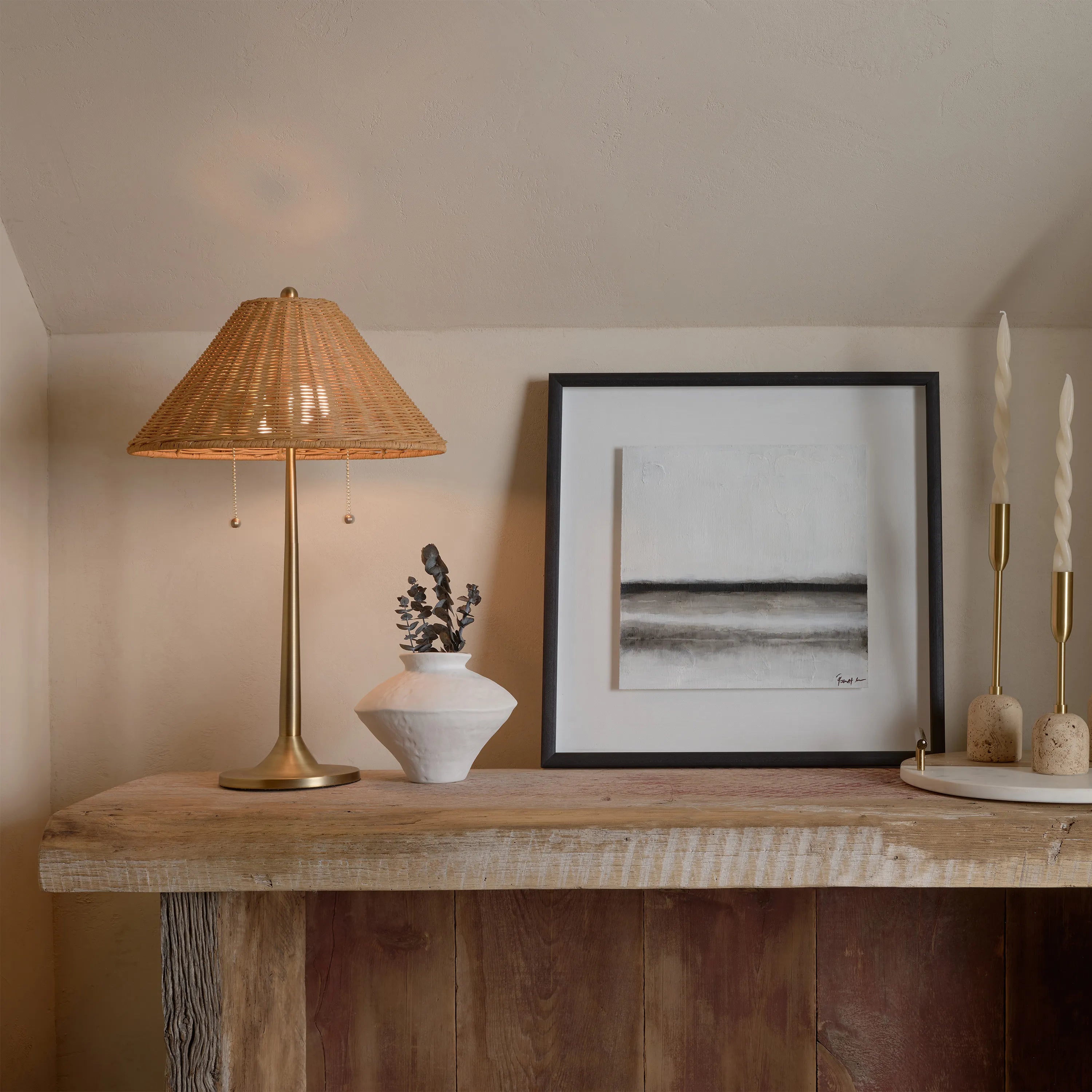 Solara Rattan Glow Table Lamp styled on rustic wood console beside artwork and decor pieces