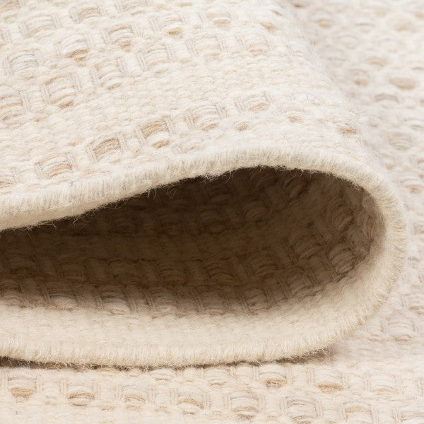 Folded edge view of the ivory Theo wool rug, demonstrating the thick woven pile and reversible hand-woven construction without canvas backing.