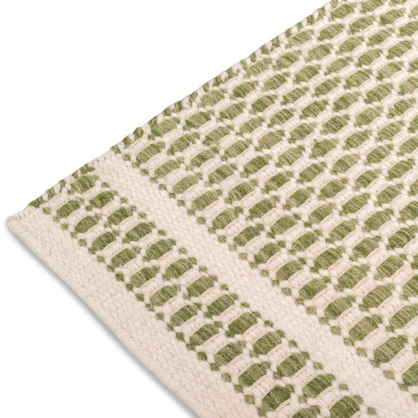 Close-up of the woven edge and border detailing on the sage green and cream Theo hand-woven wool rug.