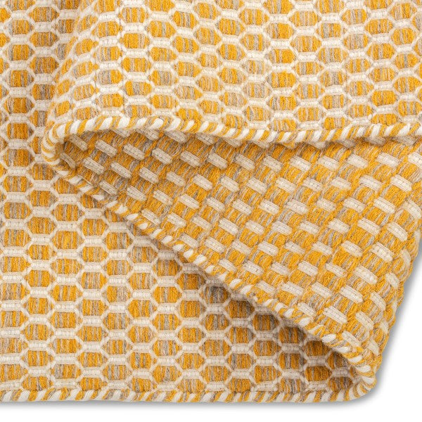 A folded corner of the yellow Theo hand-woven wool rug, showing its thickness, durable backing, and soft texture.