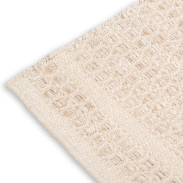 Close-up corner detail of the ivory Theo wool rug showing the neat edge binding and chunky woven texture.