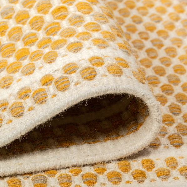 Draped folds of the mustard yellow Theo wool rug highlighting the flexible, soft texture of its geometric pattern.