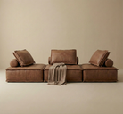 Brown sectional sofa with cushions and a blanket on a beige background