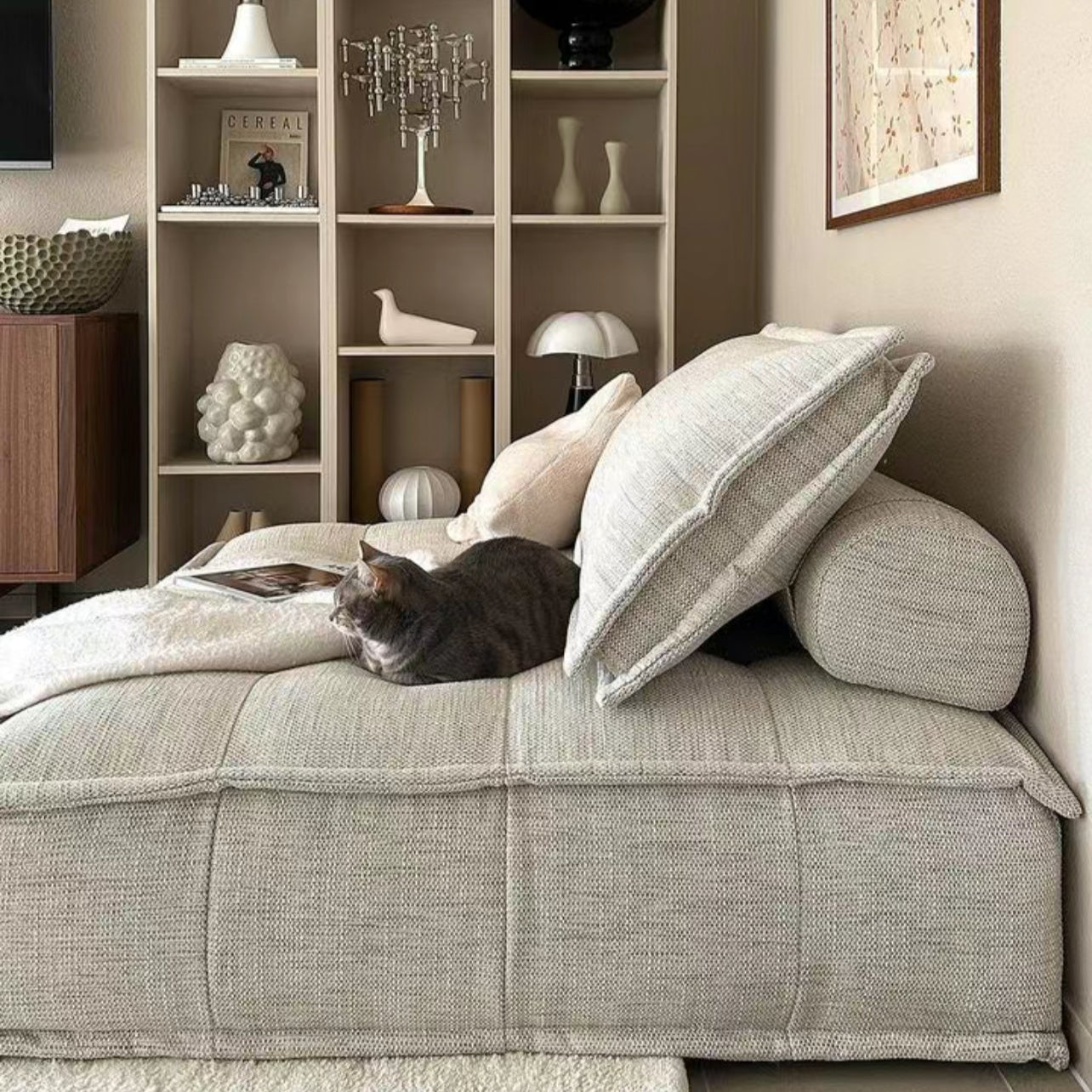 Side view of Tofu Modular Sofa in linen fabric with a cat lounging on top, styled in warm neutral living space with bookshelf decor