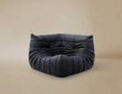 Dark grey TOGO Lounger corner chair showing deep tufted folds and low profile floor seating design.