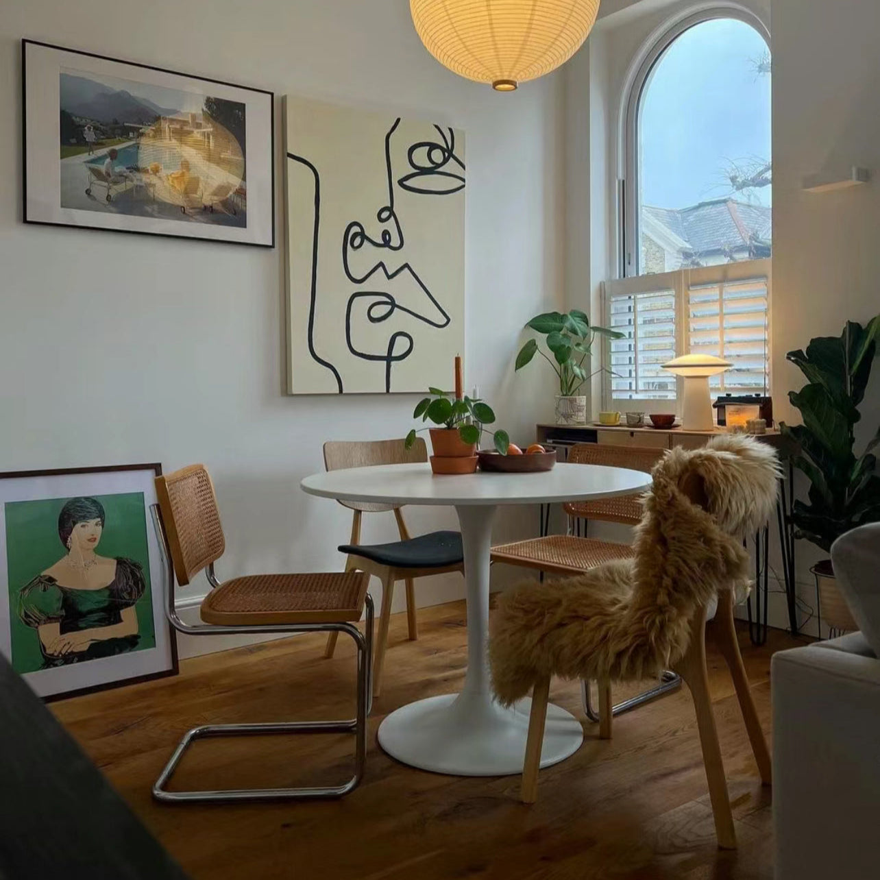 Tulip Dining Table styled in a cozy modern dining nook with warm wood flooring, rattan chairs, and abstract wall art