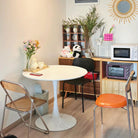 Tulip Dining Table styled in a cozy dining nook with mixed chairs, flowers, and wooden shelves for a warm home ambiance