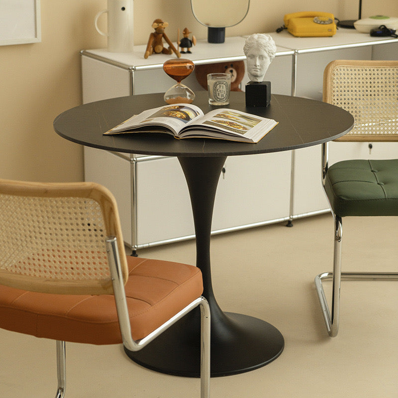 Black Tulip Dining Table styled in a cozy studio corner with rattan and leather chairs and open book on tabletop