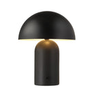 Lit view of the Umbra black metal table lamp casting a warm downward glow from its dome shade.
