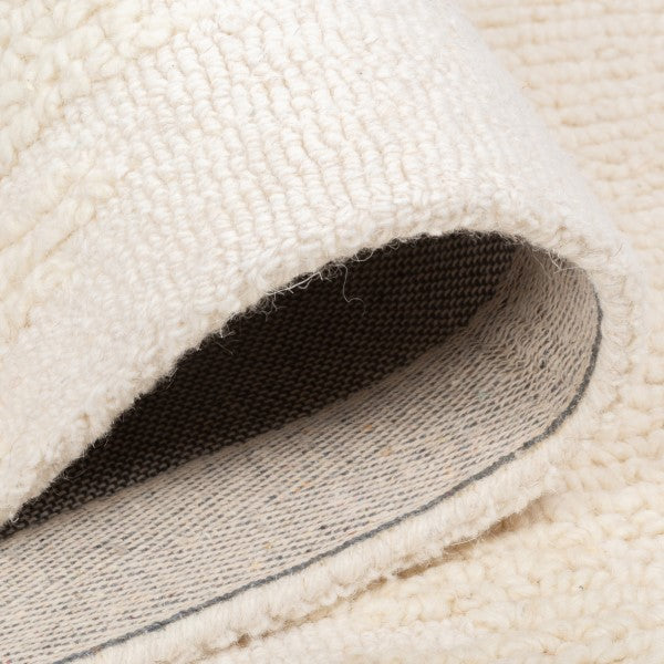 Folded corner of the vinne wool rug revealing the durable grey canvas backing typical of high-quality hand-tufted construction.