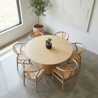 Round wooden table with six chairs in a modern room with a plant and window.