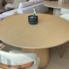 Willow Ridge round dining table in solid ash wood displayed in showroom with cream chairs